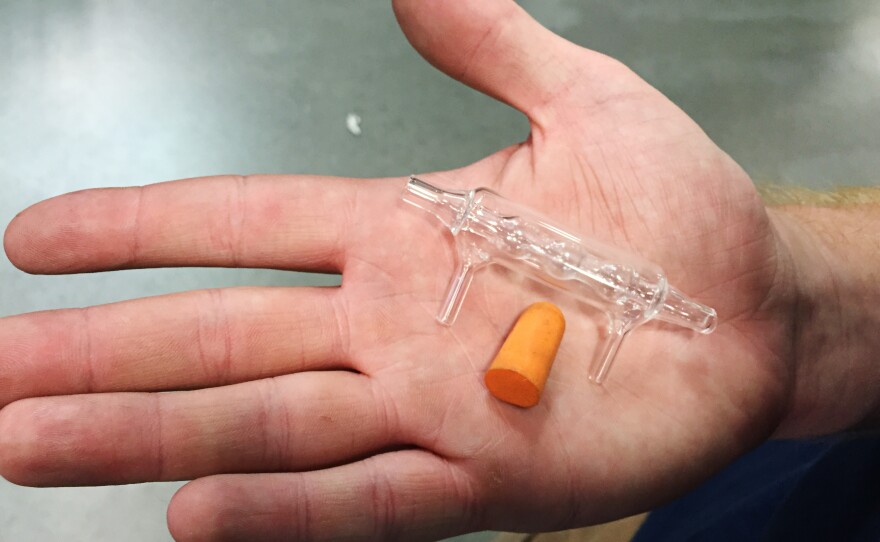 Neil Messinger holds a glass bubble condenser he created and a foam ear plug in his hand for size comparison.