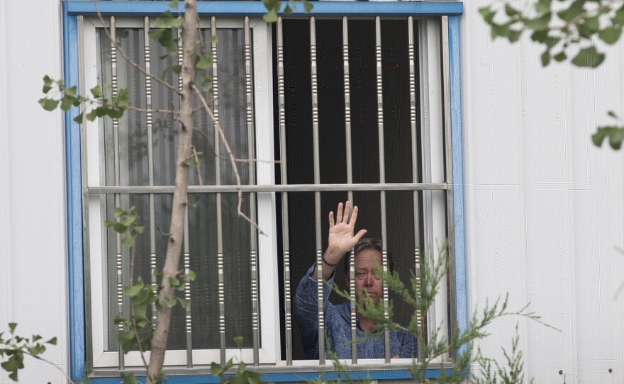 American Chip Starnes, co-owner of Specialty Medical Supplies, waves Monday from a window where he is being held by angry workers inside his plant at the Jinyurui Science and Technology Park on the outskirts of Beijing. He remained confined to the plant on Wednesday.