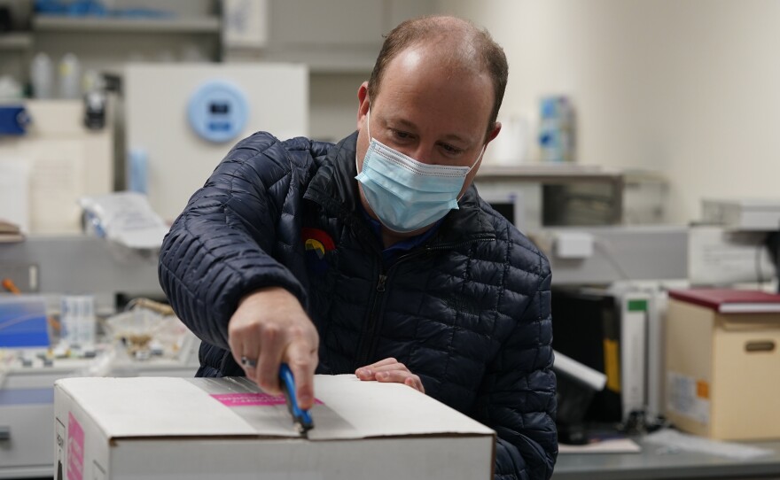 Colorado Gov. Jared Polis opens the shipping box containing the state's first shipment of COVID-19 vaccine at the Colorado Department of Public Health and Environment, Dec. 14, 2020, in east Denver.