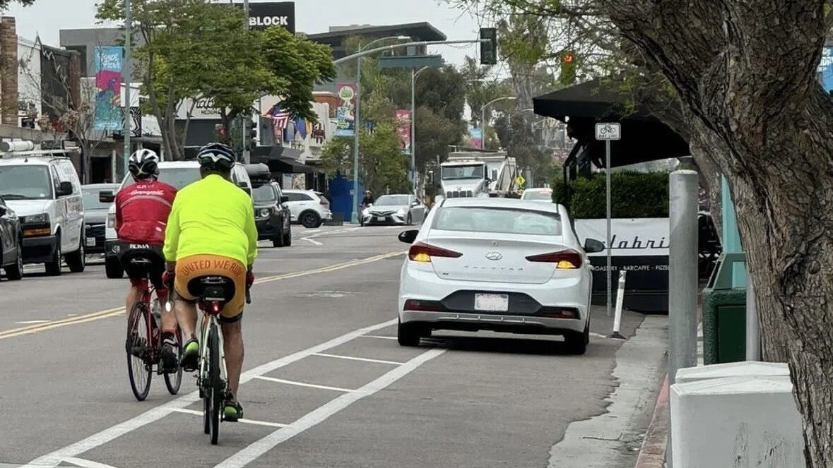 Two cyclists ride past a car parked in the bike lane of 30th Street in North Park.