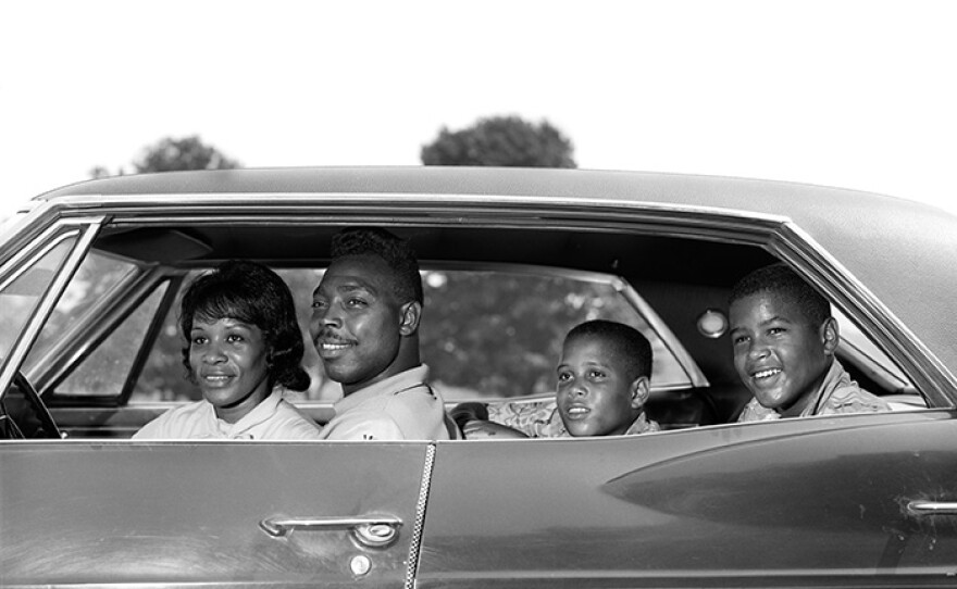 1960s, side view African American family - father, mother with two sons sitting in four-door sedan automobile.