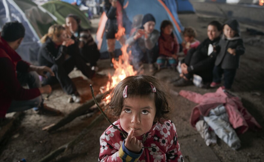 At the northern Greek border point of Idomeni on Friday, a migrant child eats as others sit around a fire in a railway-repairs hangar where people have set up their tents.