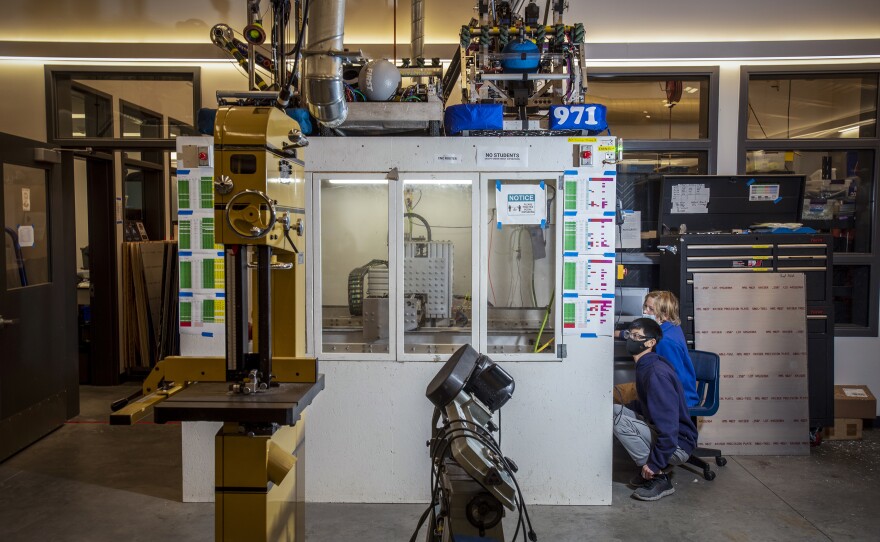 Sophomores Adriel Lim and Daniel Kessens monitor the progress of the CNC (computer numeric control) router in the Spartan Robotics machine shop, which also serves as a repository for Team 971's previous robots above.