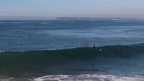 A surfer floats along the top of a wave at Imperial Beach on Monday, Dec. 2, 2024.
