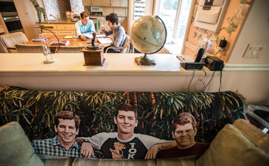 Charles (right) gets tutoring from his brother David on the GRE test at their parents' home. The couch in the living room bears a blanket with images of the three Mayer brothers.