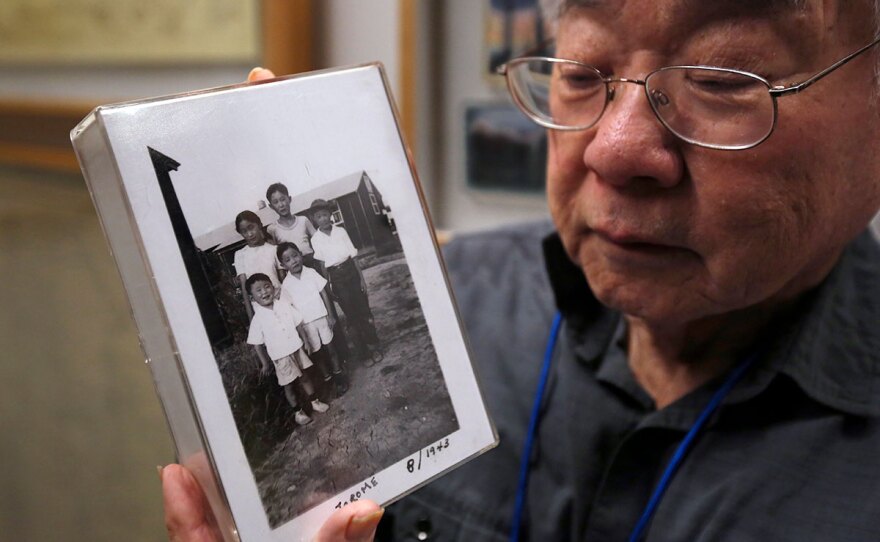 In this photo taken Tuesday, Feb. 11, 2020, Les Ouchida holds a 1943 photo of himself, front row, center, and his siblings taken at the internment camp his family was moved to, as he poses at the permanent exhibit titled "UpRooted Japanese Americans in World War II" at the California Museum in Sacramento, Calif.