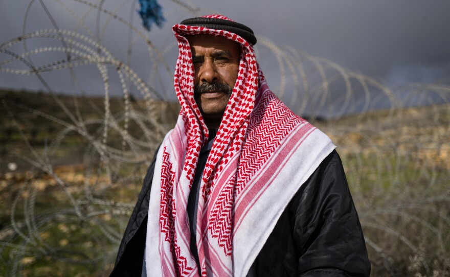 Sakher Abu Dahouk in front of the razor wire of the separation barrier that surrounds his land in Beit Hanina Al-Balad in the Israeli-occupied West Bank. His extended family has moved several times since 1948, as Israel seized territory in subsequent wars, redrew boundaries and built more Jewish settlements. "We still have deeds to our land," in what's now southern Israel, he says.