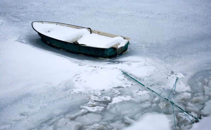 En ensom robåd sidder fast i isen i en havn i Nuuk.