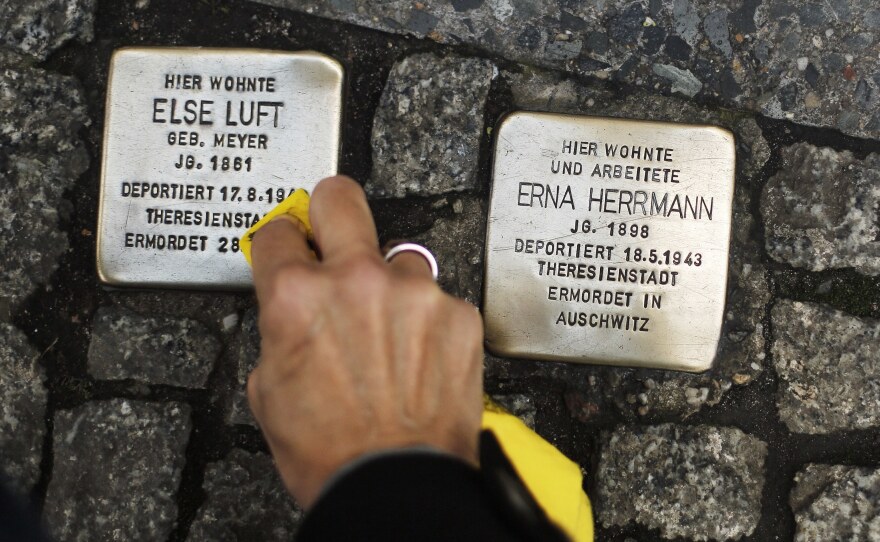 A woman cleans a Stolperstein, or "stumbling stone," placed in the sidewalk in front of houses where victims of the Holocaust lived before they were deported and killed by the Nazis.