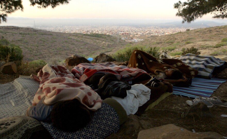 Moneba (left) sleeps beside fellow migrants he calls his "brothers" in a hidden forest camp in Morocco. He was the chief of about 100 boys and young men from Guinea who hoped to reach Europe. The Spanish enclave of Melilla and the Mediterranean Sea are both visible in the distance.