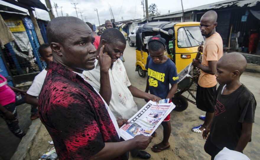 Residents gather on the main road to read newspaper headlines about Ebola.