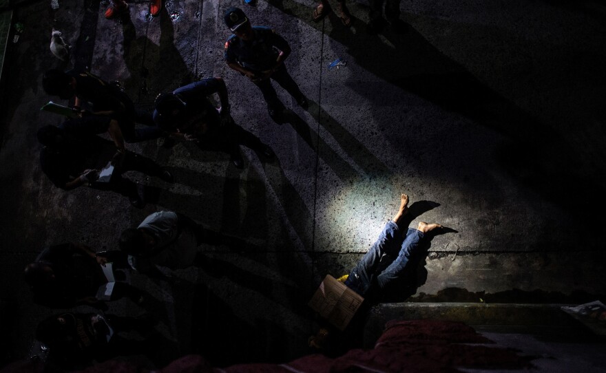 Police officers examine the body of an alleged drug dealer on a street in Manila in July, his face covered with packing tape and a placard that read, "I'm a pusher."