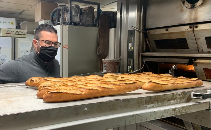 Tony Doré wears a face mask as baguettes cool in his bakery in Paris' 15th arrondissement.