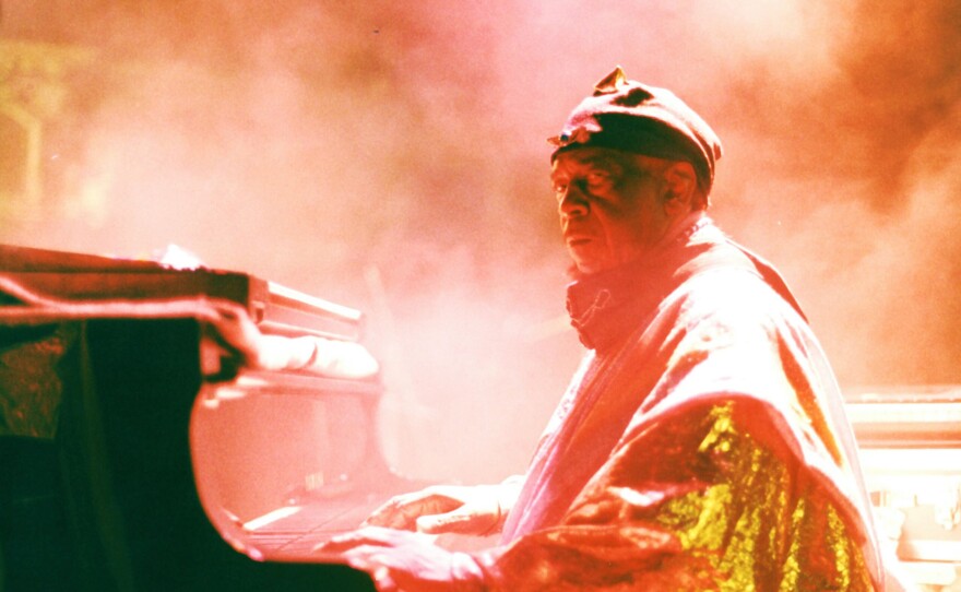 Sun Ra in orange light and haze plays piano and glares at camera.
