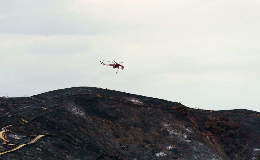 A firefighting helicopter flies over burned hills during the La Tuna fire in Los Angeles, California on Sunday.