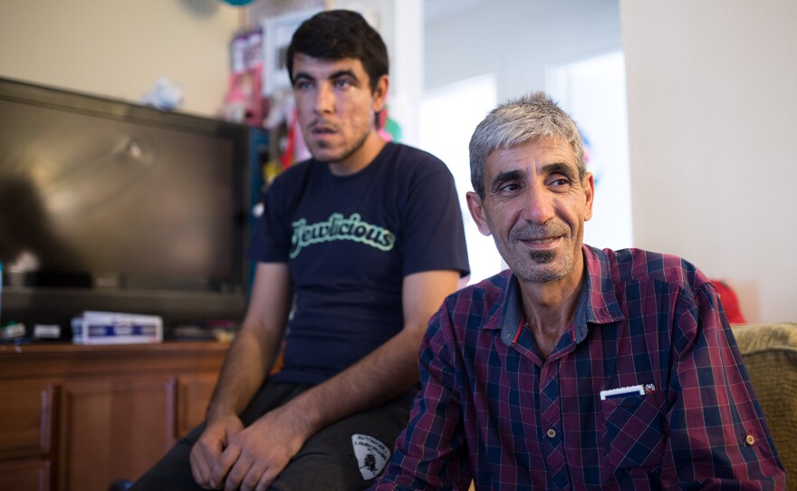 Mahmoud Alibrahim, (right), sits with one of his older sons on a couch in the living space of his family's two-bedroom El Cajon apartment, July 25, 2017.