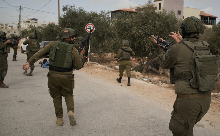 Israeli soldiers move toward a Palestinian man lying wounded on a road after they shot him following a settler attack on Palestinians harvesting olives in the West Bank village of Abu Falah, Friday.