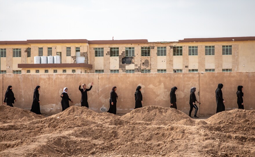 A procession of survivors makes its way to mass graves near the village of Kocho containing the bodies of their loved ones, on the fifth anniversary of the start of the ISIS genocide against Yazidis. ISIS rounded up everyone in the village at gunpoint in the school past the wall, shooting men and older boys and taking women and children captive.