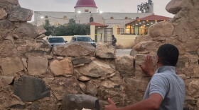 A man looks through a gap in a stone wall toward a Greek Orthodox church where gunmen opened fire during a funeral hours earlier in Hamoud village, in Jordan's Karak governorate on Friday.