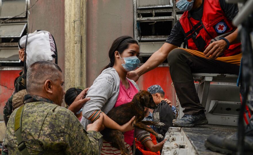 Rescue workers help a resident and her dog onto a truck as they evacuate to a safe area in Talisay town on Monday.