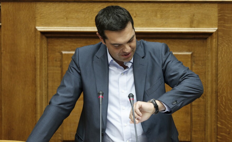 Greek Prime Minister Alexis Tsipras looks at his watch as he speaks to a marathon parliamentary session in Athens, on Friday. A bitterly divided parliament approved a draft bailout agreement with international lenders.