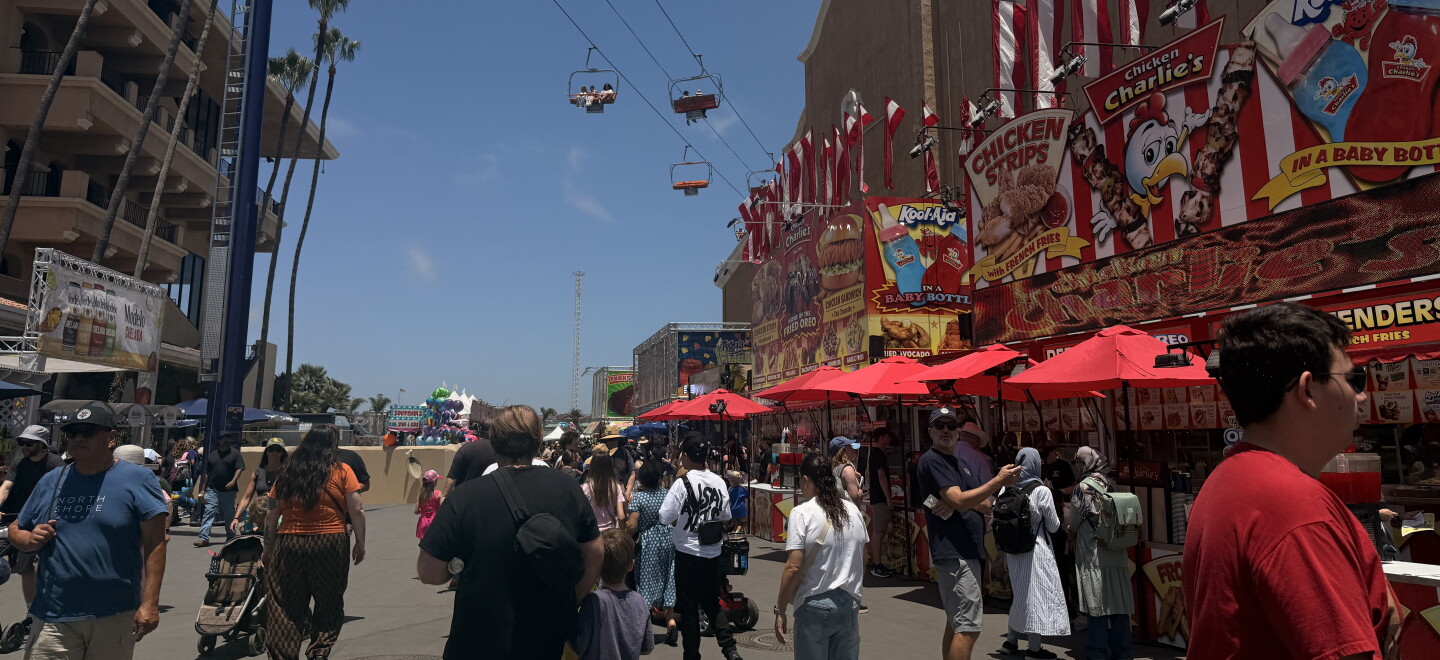 Visitors walk down a food-vendor lined walkway as the gondola ride passes overhead at the San Diego County Fair on June 10, 2026.
