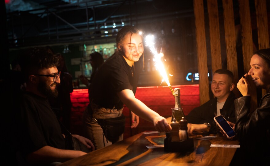 A server lights a sparkler on a bottle of champagne as she delivers it to a table.