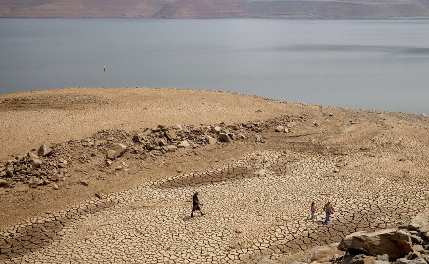 In this Aug. 22, 2021, file photo, a family walks over cracked mud near Lake Oroville's shore as water levels remain low due to continuing drought conditions in Oroville, Calif.