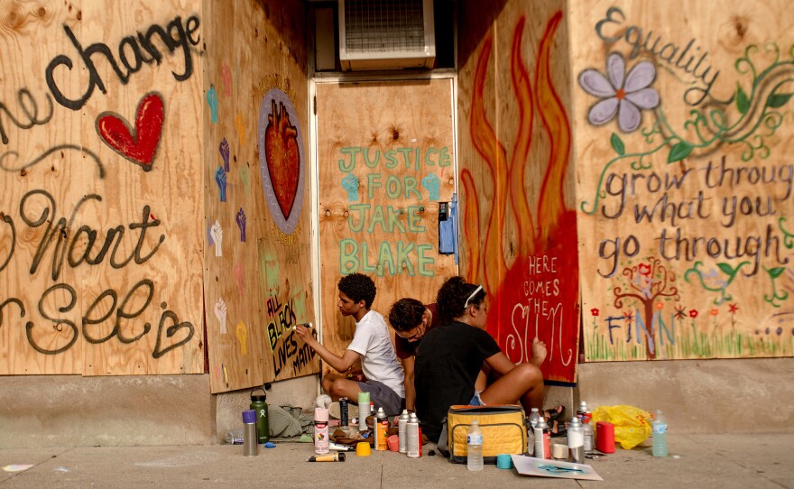 Kenteay Varnell, Mya Wilson, and Zipporah Gordon paint a mural on the boarded windows and door of a business.