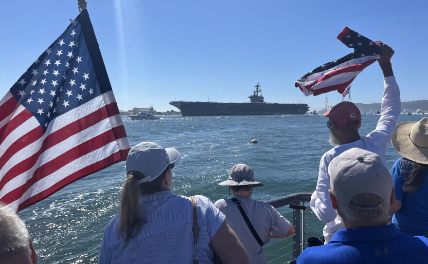 People gather with American flags along Shelter Island's shoreline ahead of the USS Lincoln's arrival, Oct. 8, 2026.