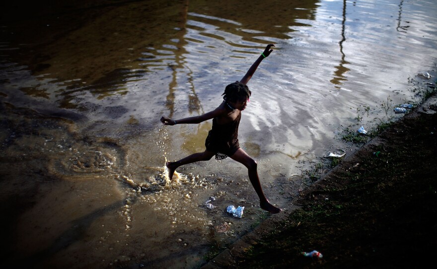 A little girl jumps across a flooded field containing the sewage runoff from the Mais Gate Camp after heavy rains in Port-au-Prince in 2010.