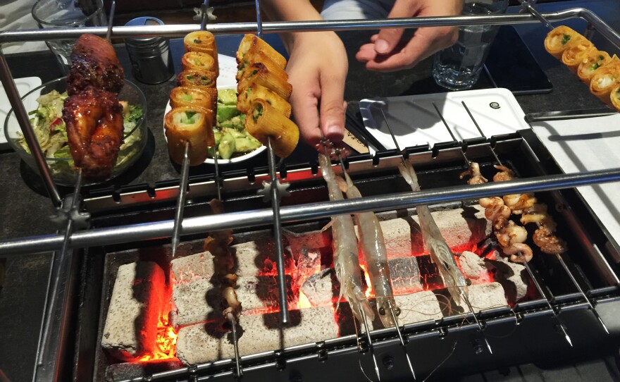 Food on skewers cooks over hot coals at the caveman-themed A Very Long Time Ago restaurant.