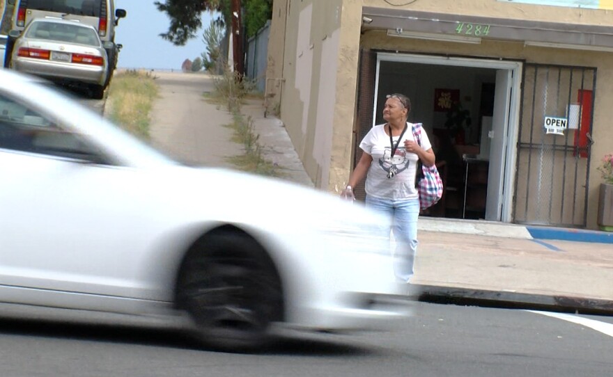 A car drives by as a woman waits to cross Market Street in southeastern San Diego, Sept. 1, 2016.