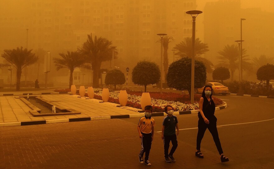 A woman and two children wear medical masks as they cross a street amid a sandstorm in Dubai.