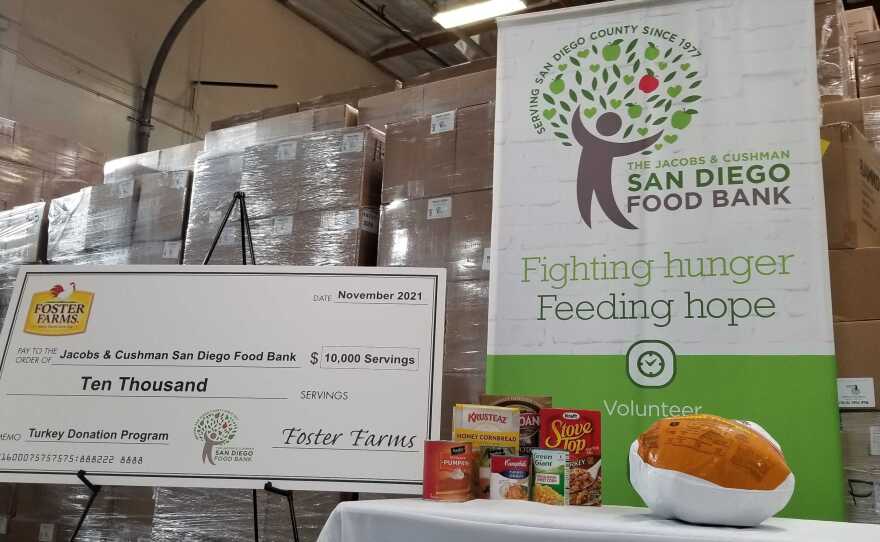 A Foster Farms turkey donation check displayed with a San Diego Food Bank sign and Thanksgiving food examples, including a frozen turkey at the San Diego Food Bank on Nov. 16, 2021.