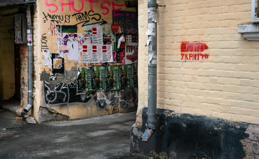 A sign with red lettering and an arrow painted onto the wall next to an alley indicates a shelter is nearby.