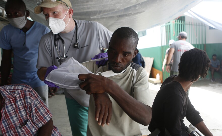 Andrew Patterson with the aid organization Give Hope wraps a sling around John Sanozier for his injured shoulder.