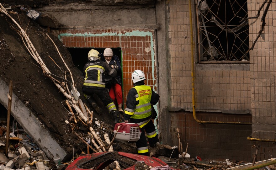 Firefighters help a woman climb out of the building after she went inside to search for her cat, following the missile strike.