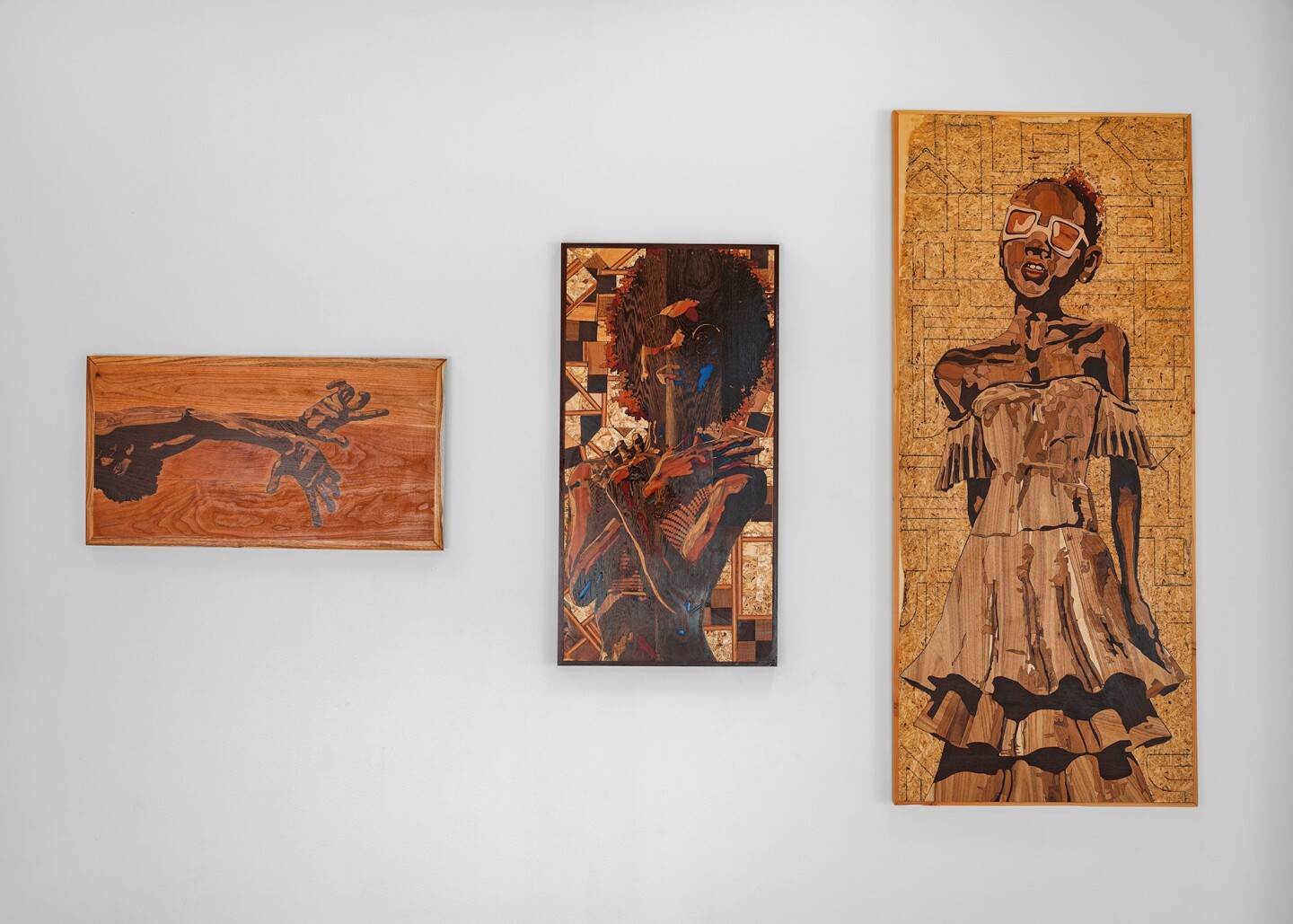 Flat, 2-dimensional wooden sculpture-paintings feature hands, and portraits. 