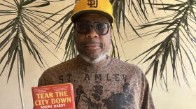 The image is a photograph of author and former NFL player Andre Hardy, as he holds up his novel "Tear the City Down" at KPBS on September 1, 2026.