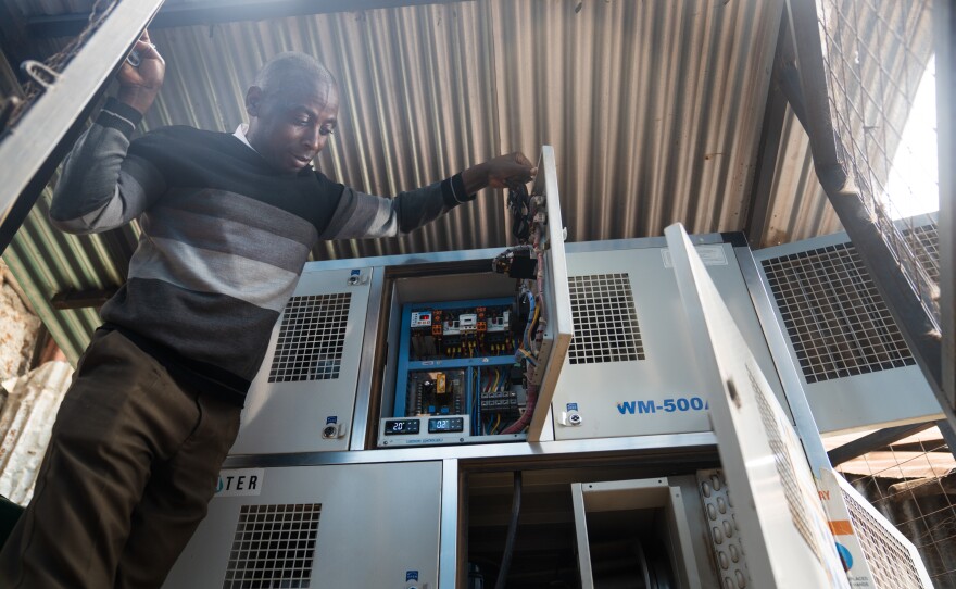 The teacher Musonye shows the air-to-water system that was installed at the school. It uses fans to suck in hot, moisture-filled air, and then cools the air to condense the water – much like a dehumidifier or an AC unit. The water is then filtered and minerals are added, making it safe for drinking.