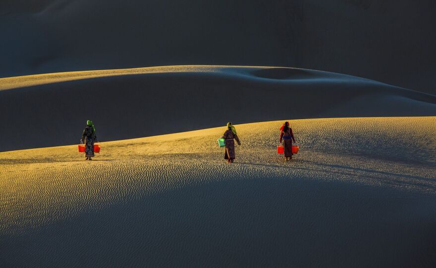 As the sun rises over the Naiman Desert in Inner Mongolia, China, girls carry buckets on their way to get water.