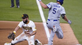 San Diego Padres' Eric Hosmer, left, tries to control the ball as Los Angeles Dodgers' Corey Seager (5) safely reaches first on a throwing error by Fernando Tatis Jr. during the third inning in Game 3 of a baseball National League Division Series Thursday, Oct. 8, 2020, in Arlington, Texas. 