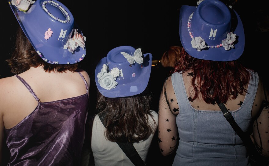 Three fans show off their BTS hats as they wait for the first BTS in person concert in two years.