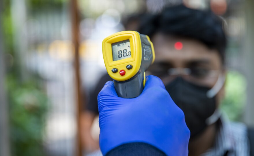 An office worker is screened with an infrared thermometer as he enters a building in New Delhi, India.