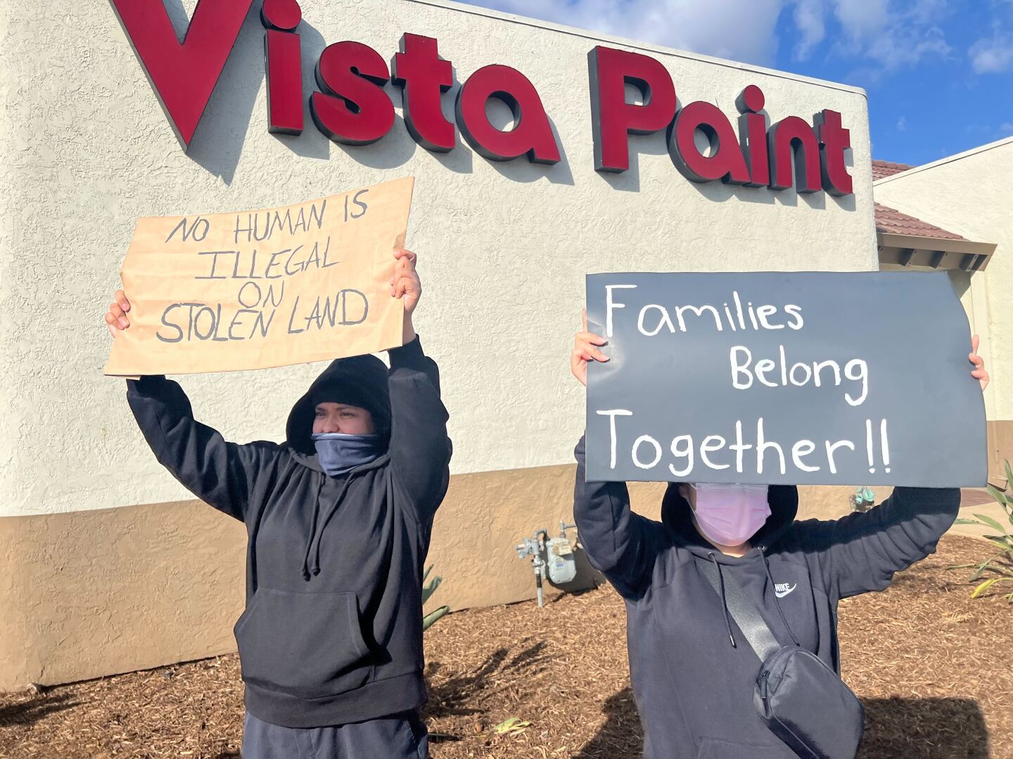 Two protesters hold signs reading "No human is illegal on stolen land" and "Families belong together" during a protest at Washington Avenue and Escondido Boulevard in Escondido on Jan. 29, 2025.